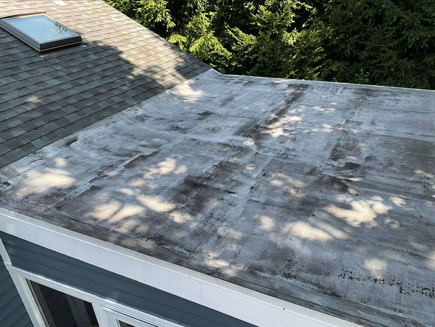 Stained low-slope roof membrane beside a shingled roof slope with a skylight