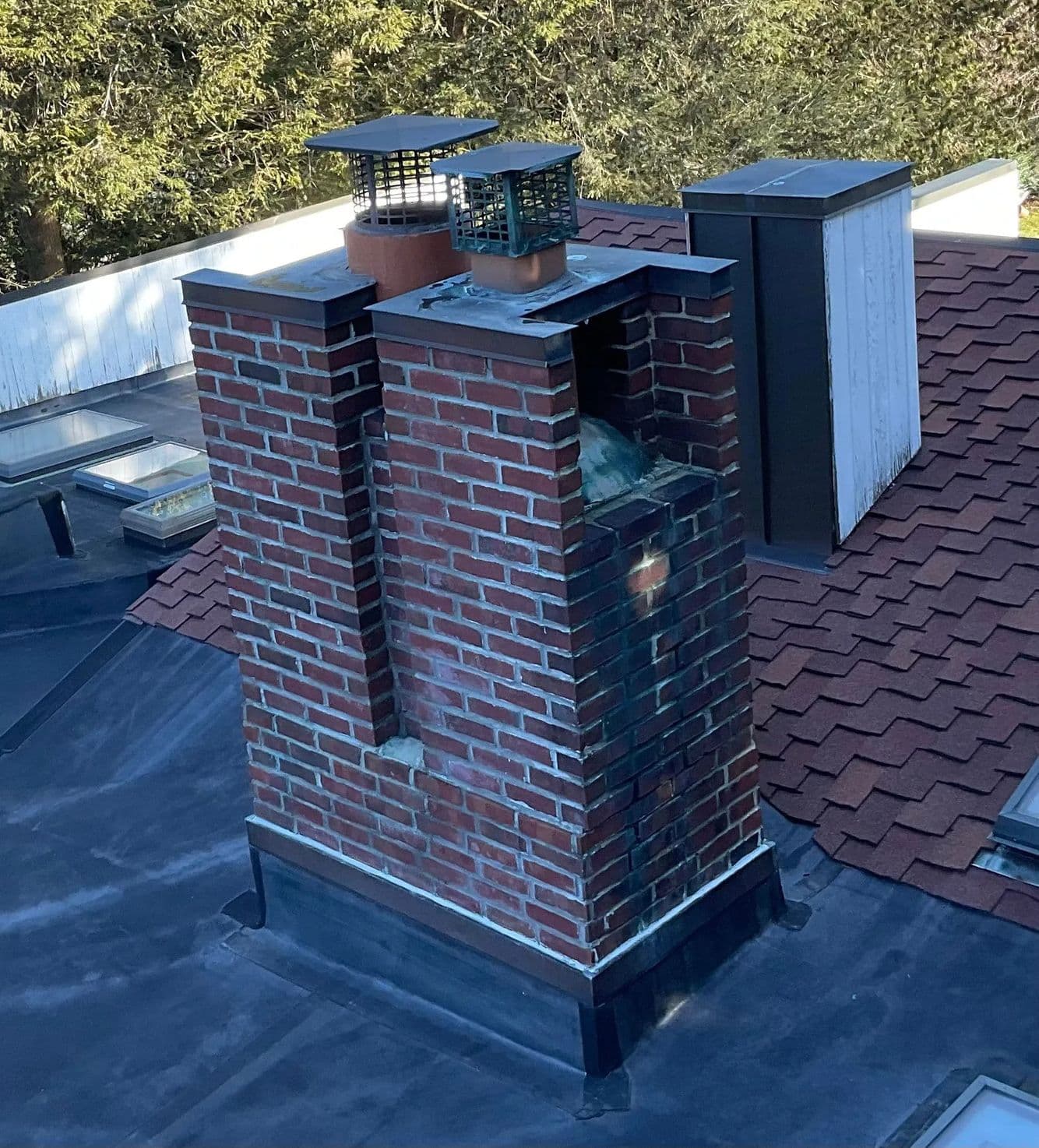 Brick chimney with two mesh-capped flues on a flat roof and an open gap in the brickwork near the top