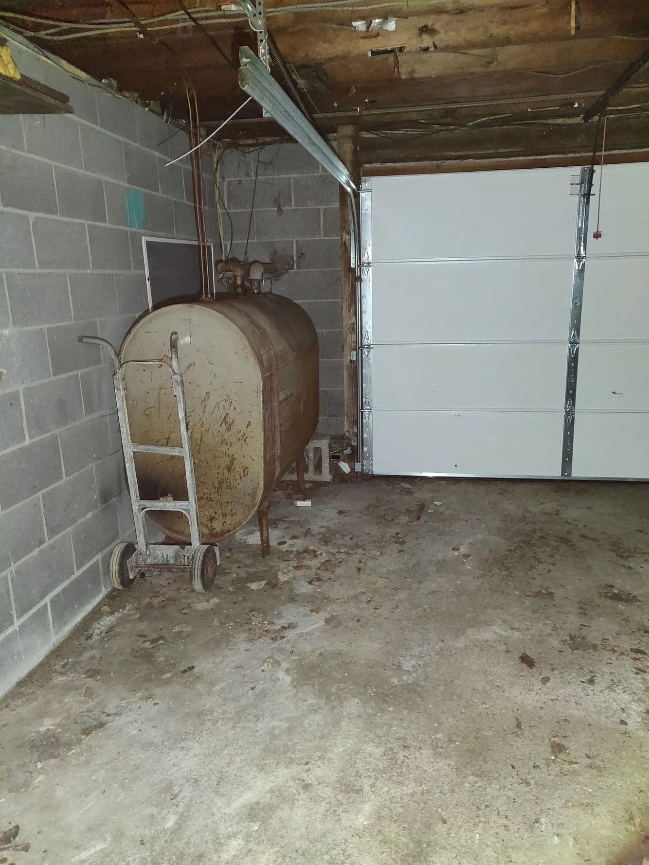 Rust-marked oval steel tank on legs in a garage with block walls, a hand truck beside it