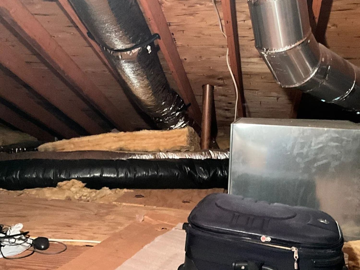 Attic with foil and black flexible ducts, a metal duct box and loose fiberglass insulation on the floor