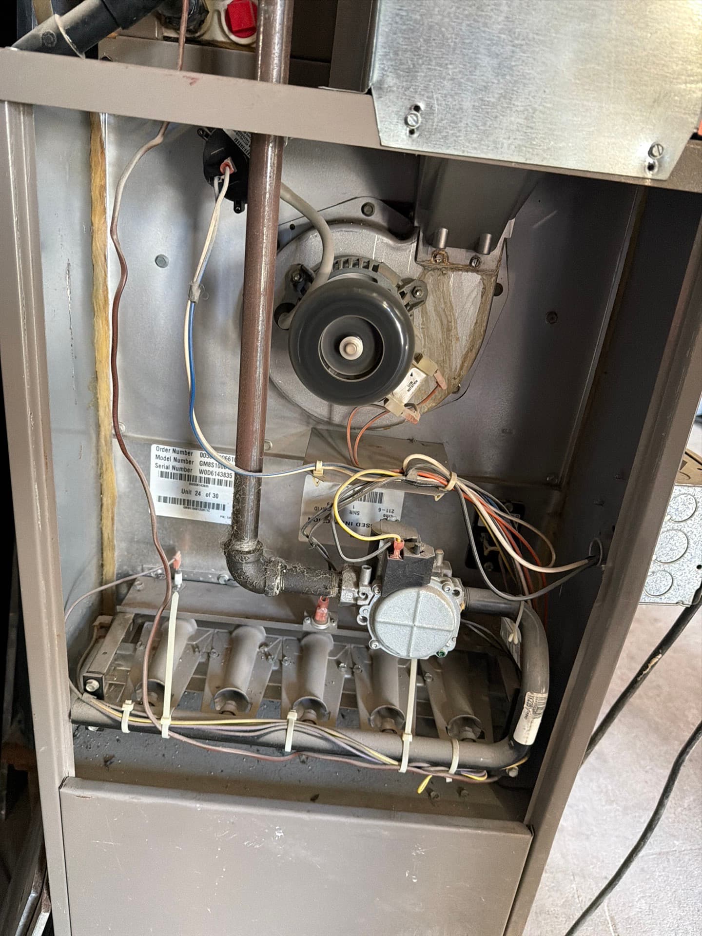 Gas furnace with its front panel removed, showing the burners, gas valve, inducer fan and dust on the gas pipe