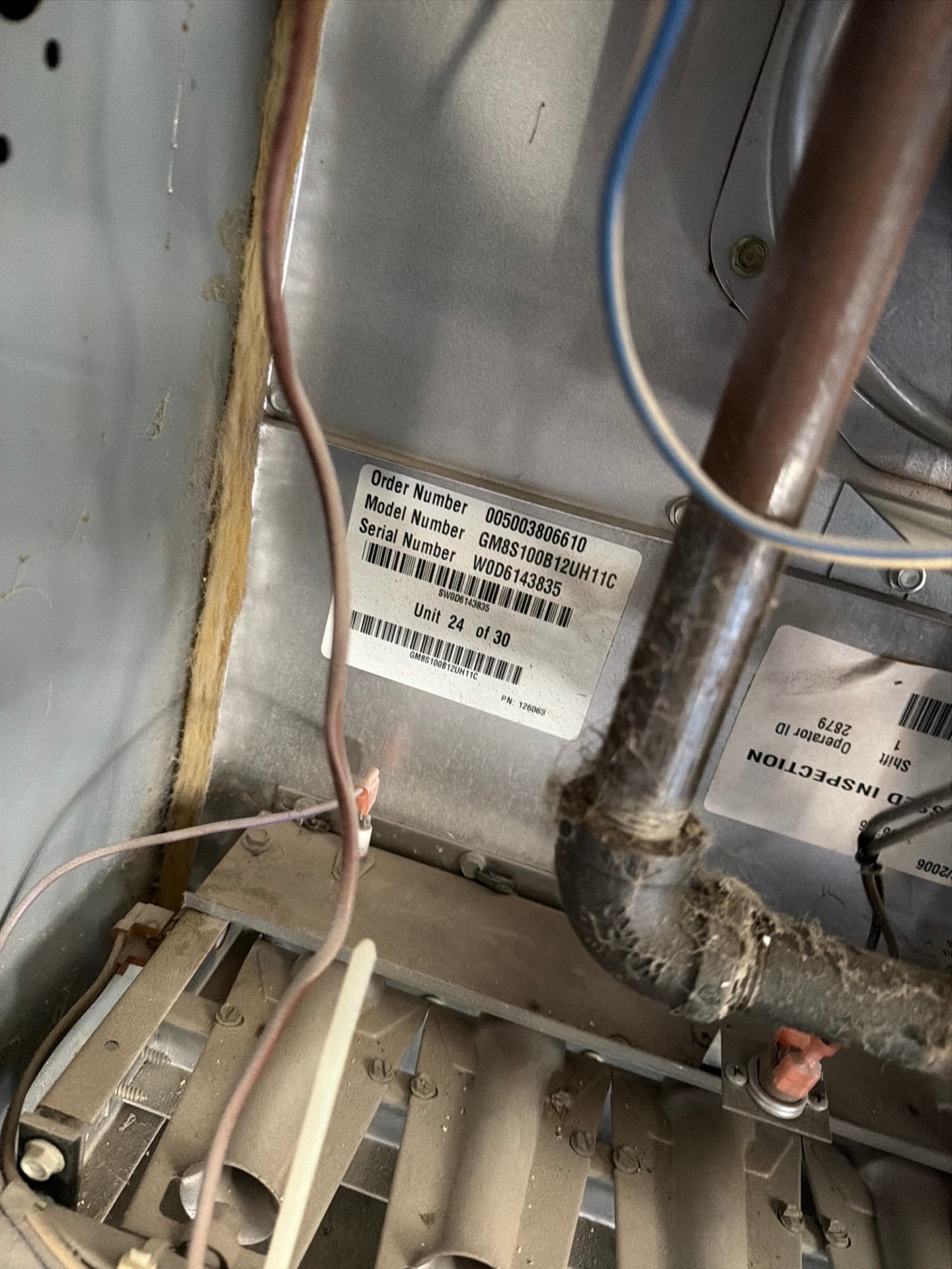 Furnace data label showing order, model and serial numbers, beside a dusty gas pipe and burner assembly