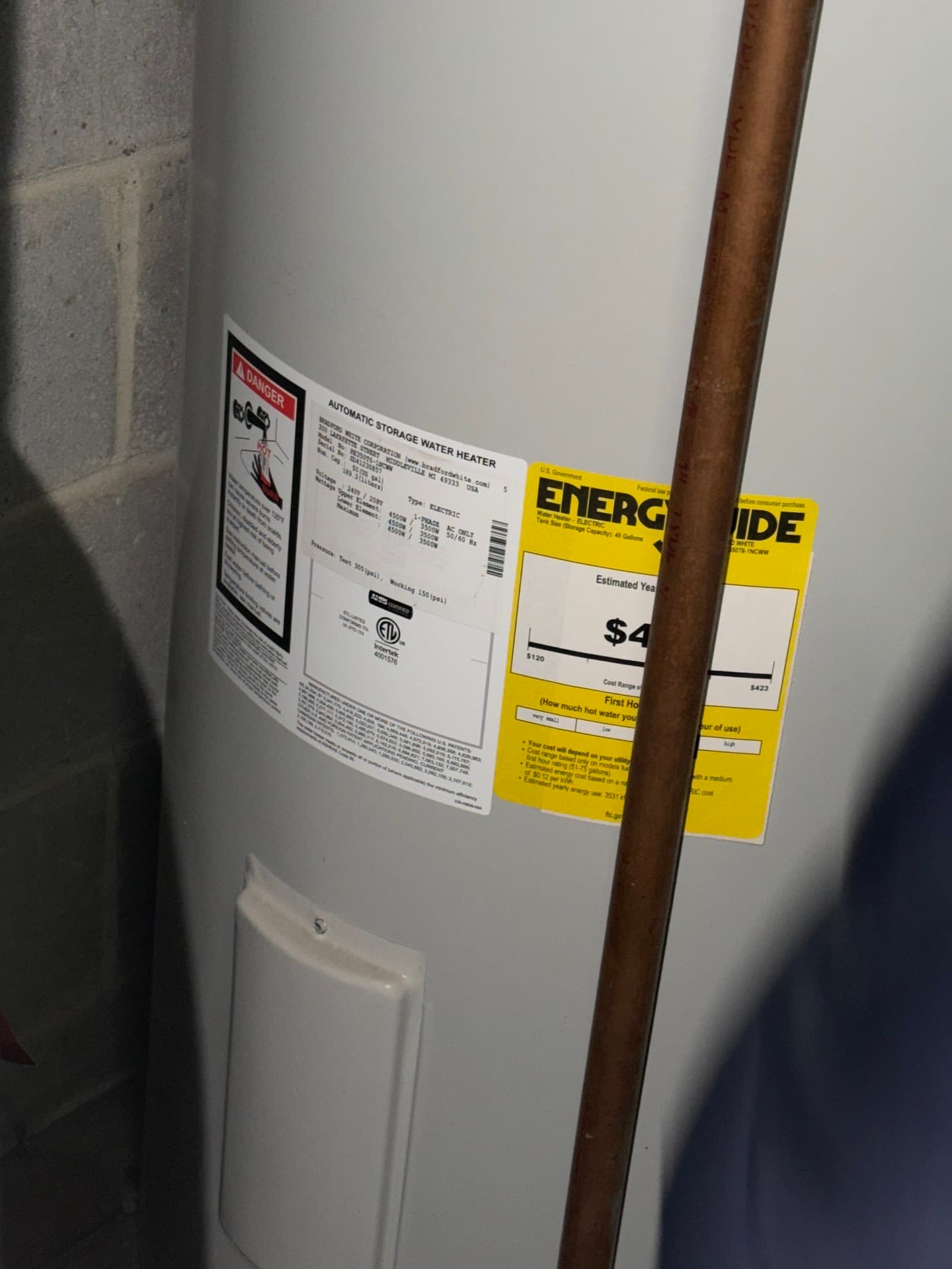 Electric storage water heater with its rating label and yellow EnergyGuide label, a copper pipe in front