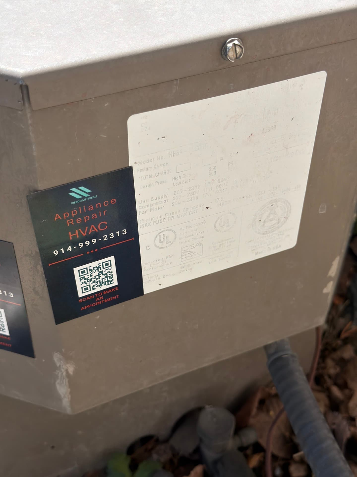 Faded, hard-to-read data plate on an outdoor AC unit, next to a repair company's sticker